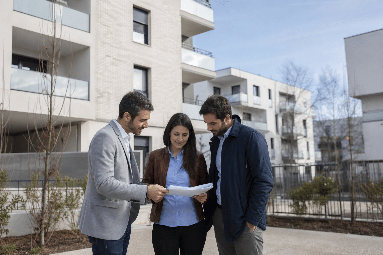 Trois personnes regardant des documents devant immeubles modernes